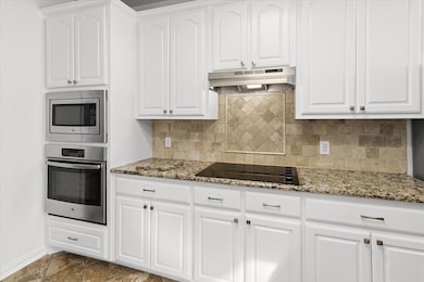 Kitchen with stainless steel appliances, white cabinets, and light stone counters