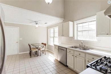 Kitchen featuring appliances with stainless steel finishes, a sink, crown molding, light tile patterned flooring, and white cabinetry