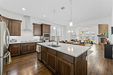 Kitchen with wall chimney range hood, dark wood-type flooring, stainless steel appliances, sink, and ceiling fan