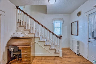 Entrance foyer with radiator heating unit, a textured ceiling, wood finished floors, a textured wall, and stairs