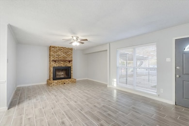 Unfurnished living room featuring ceiling fan, a textured ceiling, a brick fireplace, and wood tiled floors