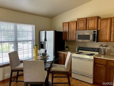 Kitchen featuring brown cabinets, white electric range oven, light countertops, stainless steel microwave, and lofted ceiling
