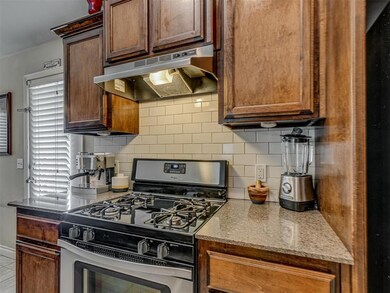 Kitchen with gas stove, under cabinet range hood, tasteful backsplash, and light stone counters