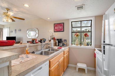 Kitchen with a textured ceiling, white appliances, light countertops, light tile patterned floors, and a ceiling fan