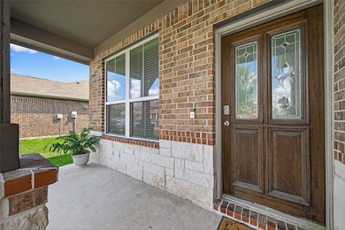 This photo showcases a welcoming front porch with a stylish wooden door featuring decorative glass panels. The brick and stone facade adds charm, while a potted plant brings a touch of greenery.