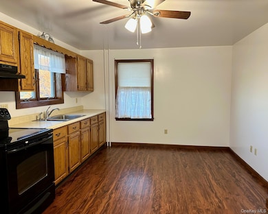 Kitchen featuring black range with electric stovetop, light countertops, dark wood-style floors, brown cabinets, and ceiling fan