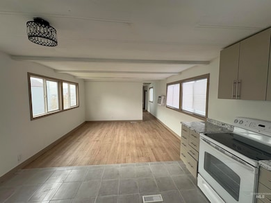 Kitchen with white range with electric cooktop, beamed ceiling, gray cabinetry, light tile patterned flooring, and dark stone countertops