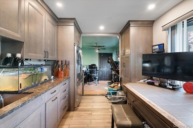 Kitchen with light wood finished floors, a ceiling fan, stainless steel fridge with ice dispenser, recessed lighting, and tile countertops
