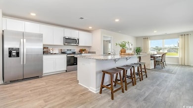 Kitchen featuring appliances with stainless steel finishes, a kitchen breakfast bar, light wood-style flooring, light stone counters, and recessed lighting