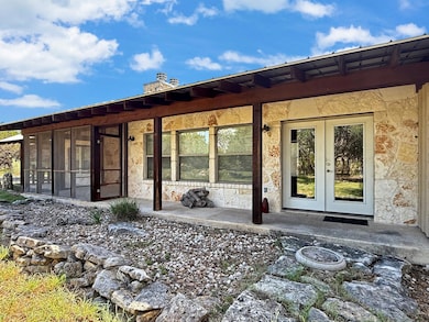 Rear view of house with french doors, a sunroom, stone siding, and a chimney
