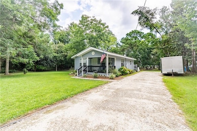 View of front of house with dirt driveway, covered porch, a front lawn, and view of scattered trees