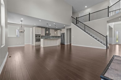Unfurnished living room with stairs, a high ceiling, dark wood-style floors, recessed lighting, and a chandelier