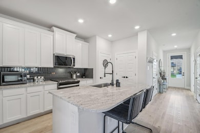Kitchen featuring a kitchen bar, light wood-type flooring, tasteful backsplash, gas range oven, and stainless steel microwave