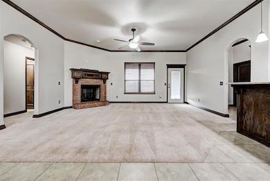 Unfurnished living room featuring arched walkways, ornamental molding, light colored carpet, a fireplace, and a ceiling fan