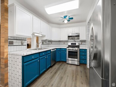Kitchen featuring blue cabinets, appliances with stainless steel finishes, white cabinets, light wood-type flooring, and decorative backsplash
