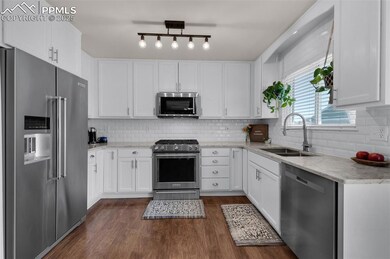 Kitchen with stainless steel appliances, white cabinetry, and dark wood-style floors