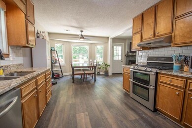 Kitchen with appliances with stainless steel finishes, under cabinet range hood, brown cabinetry, dark wood-type flooring, and a textured ceiling