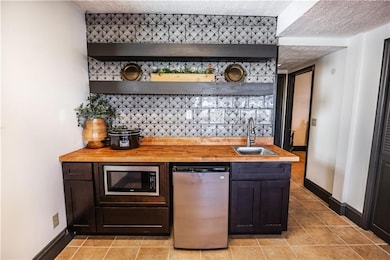 Bar featuring fridge, stainless steel microwave, a textured ceiling, a sink, and indoor wet bar