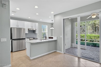 Kitchen with appliances with stainless steel finishes, white cabinets, decorative light fixtures, backsplash, and light stone counters