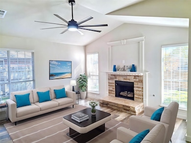 Living room featuring wood finished floors, healthy amount of natural light, lofted ceiling, a stone fireplace, and a ceiling fan