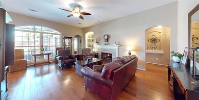 Looking into the family room, you can see the lighted ceiling fan, wood floors and on the right , the hallway to the secondary bedrooms with its art niche.