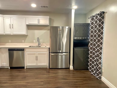 Kitchen with stainless steel appliances, white cabinets, dark wood finished floors, and stacked washer / drying machine