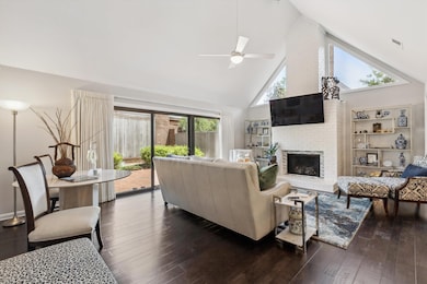 Featuring a Vaulted Ceiling w/Modern Fan, Painted Brick Fireplace with Gas Logs, Wide Plank Hardwood   Flooring, & Dramatic Triangular Transom Windows. Oversized Sliding Glass Doors Offer Easy Access to the Private Patio & Fill the Room w/Natural Lig