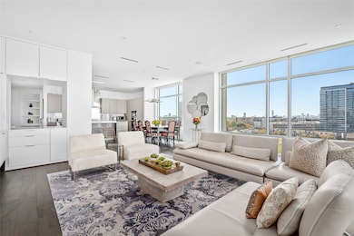 Beautifully illuminated by expansive windows and stunning views, the open concept creates a seamless flow from the living area into the dining and kitchen spaces.  The rooms are equipped with modern conveniences that enhance the comfort and entertainment, including automatic blinds and a Savant surround sound system. On the left, a sleek and functional dry bar area enhances the convenience and style of the layout.