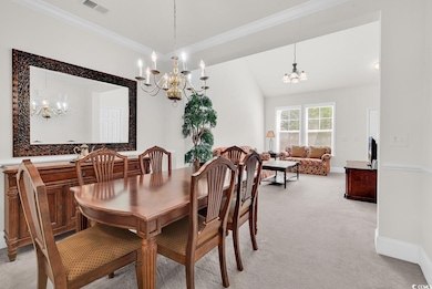 Dining space featuring a chandelier, light colored carpet, ornamental molding, and baseboards