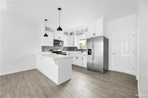 Kitchen with wood finished floors, tasteful backsplash, appliances with stainless steel finishes, and a peninsula