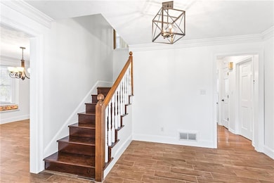 Stairs featuring a chandelier, ornamental molding, and wood finished floors