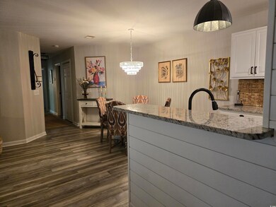 Kitchen featuring a chandelier, dark wood-style flooring, white cabinets, light stone countertops, and baseboards