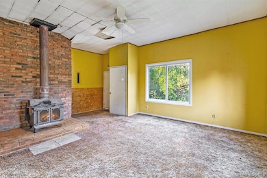 Unfurnished living room featuring a wood stove, carpet, ceiling fan, and wainscoting