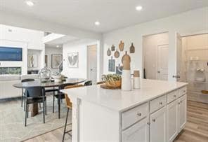 Kitchen featuring light wood-type flooring, a center island, recessed lighting, light countertops, and a breakfast bar area