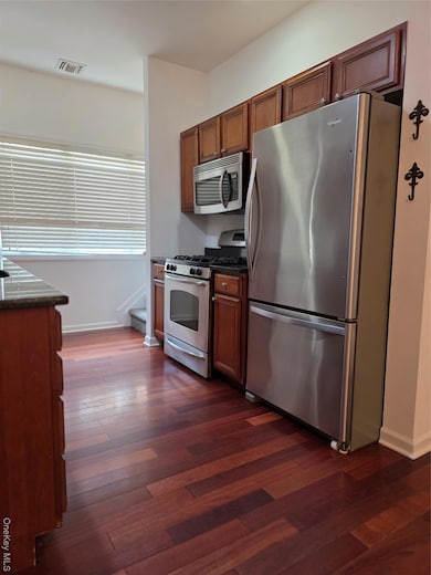 Kitchen featuring appliances with stainless steel finishes, dark wood-type flooring, brown cabinets, and dark stone counters