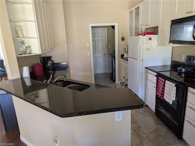 Kitchen featuring black appliances, a sink, white cabinetry, glass insert cabinets, and a peninsula
