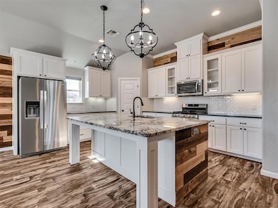 Kitchen featuring appliances with stainless steel finishes, dark stone countertops, white cabinetry, a kitchen island with sink, and tasteful backsplash
