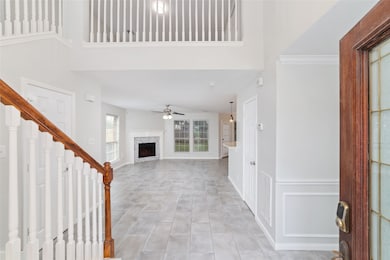 Bright and airy open-concept living area with high ceilings, a cozy fireplace, and modern tile flooring. Features a staircase with wooden accents and a view of the upstairs balcony. Ideal for comfortable living and entertaining.