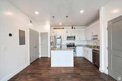 Kitchen with stainless steel appliances, light stone counters, a kitchen island, white cabinetry, and electric panel
