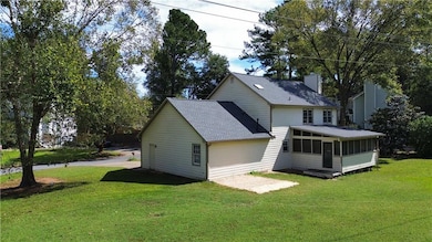 Rear view of property featuring a lawn, a sunroom, roof with shingles, and a chimney