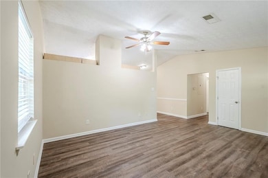 Unfurnished room featuring a ceiling fan, lofted ceiling, wood finished floors, baseboards, and a textured ceiling