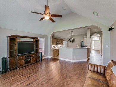 Living room featuring ceiling fan with wood-type flooring and high vaulted ceiling, open to kitchen