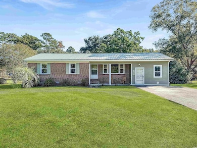 Ranch-style home with a front lawn, a metal roof, brick siding, and covered porch