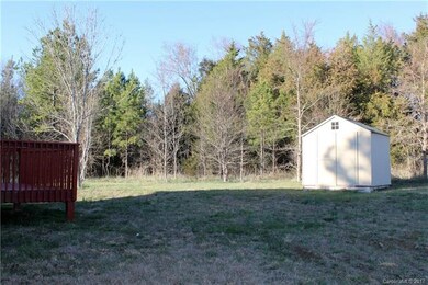 The backyard is level and bordered by trees, makin