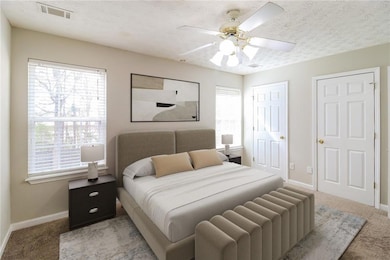 Carpeted bedroom with ceiling fan, a textured ceiling, radiator, and multiple closets