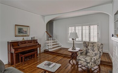 Another view of the living room with elegant arched details with a classic staircase leading to the upper level of the home. The raised area could be a great spot for a reading nook!