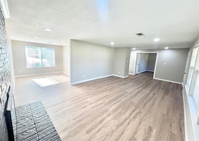Empty room with light wood-style floors, a fireplace, recessed lighting, and a textured ceiling