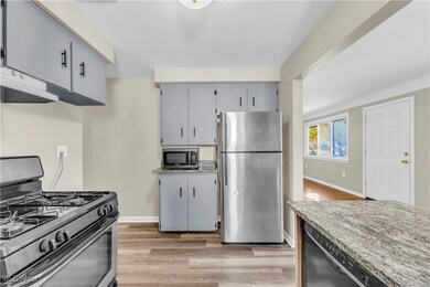 Kitchen with gray cabinetry, light stone counters, light wood-type flooring, appliances with stainless steel finishes, and exhaust hood