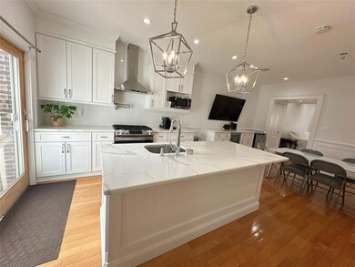 Kitchen featuring a notable chandelier, a sink, wall chimney exhaust hood, appliances with stainless steel finishes, and light wood-style floors