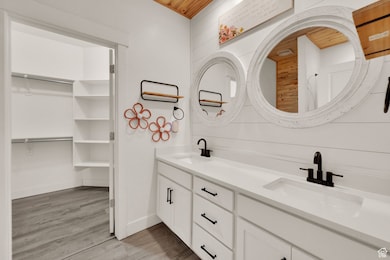 Full bath with double vanity, light wood-style flooring, and a spacious closet